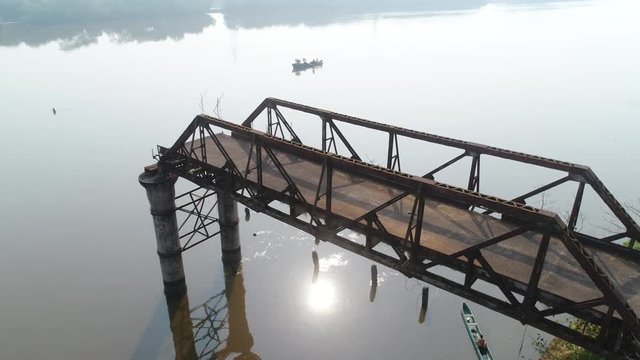 Aerial view. Flying around of supports old, rusty, dilapidated bridge over the river. Sun reflected in the water. 