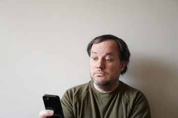 wide-eyed man looking at smartphone, sitting by wall with copy space