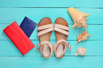 Fashionable women's sandals, passport, red purse, seashells on a blue wooden floor. The concept of...