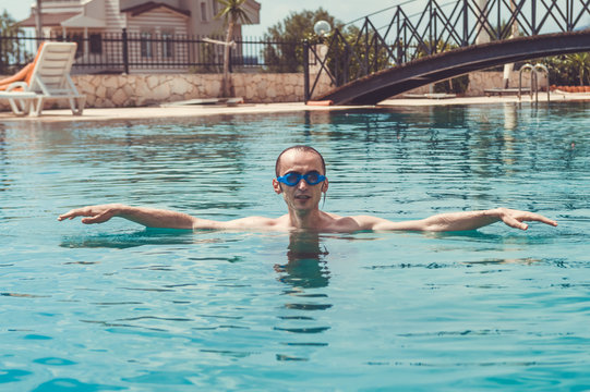 Sexy young man with goggles relaxing in the swimming pool in a resort