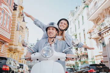 Happy couple are riding on motorcycle. Girl has put her hands on different sides of body in the air. She is looking forward and smiling. Guy is driving motorcycle. He is happy too.