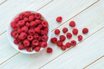White ceramic plate full of juicy ripe raspberries on a wooden white rural table.