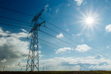 High voltage power lines and transmission towers with sunbeams in the blue sky in Normandy, France....