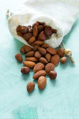 Almonds pour from sackcloth on turquoise wooden background