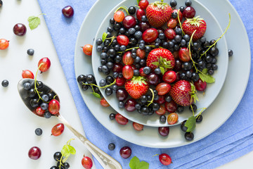 Fruit salad with strawberry, blueberry, cherry, gooseberry and black currant on wooden gray background. Flat lay. Top view