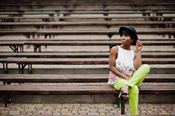Fototapeta na wymiar Amazing african american model woman in green pants and black hat posed at bench.