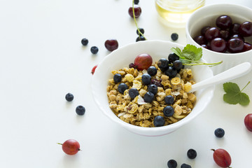 Bowl of homemade granola with strawberry, blueberry, cherry, gooseberry, black currant and honey on white wooden background. Top view. Flat lay. Copy space