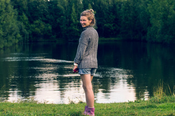 Fototapeta na wymiar Smiling woman near a pond on a background of forest in the countryside