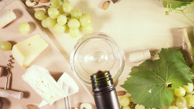 Man pours red wine into a glass from a bottle and tastes on a table cheese nuts grapes top view