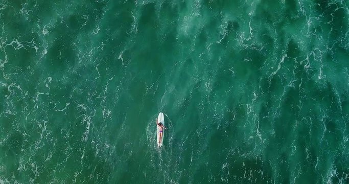 Beautiful surfer woman in sexy bikini with surfing longboard. Girl paddle on her board in big dangerous ocean waves. Modern lifestyle. People water sport camp. Extreme vacation. Aerial drone footage.