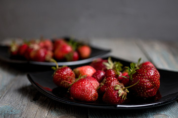 close up Red ripe strawberries on a black plates on a wooden table