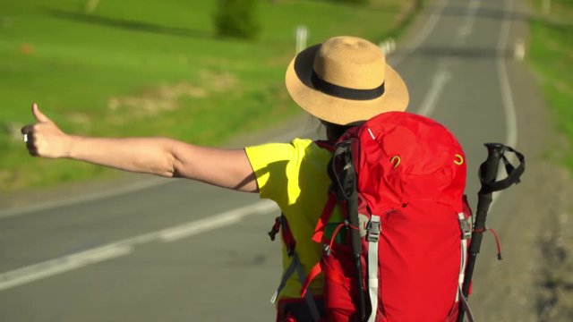 The beautiful woman in a hat with a red backpack goes along the road.