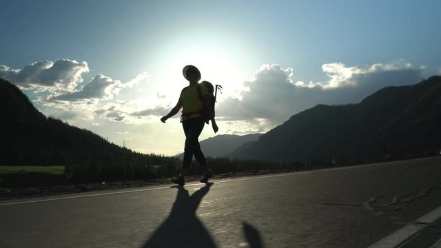 The beautiful woman in a hat with a red backpack goes along the road.