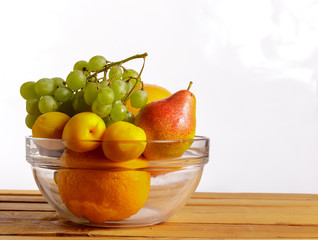 Fruit in a glass container on a wooden table on a white background.