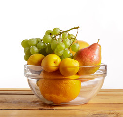 Fruit in a glass container on a wooden table on a white background.