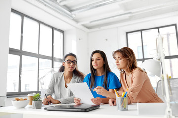 business, teamwork and people concept - female team or businesswomen discussing papers at office