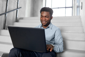 business, people and technology concept - african american businessman with laptop working computer at office stairs