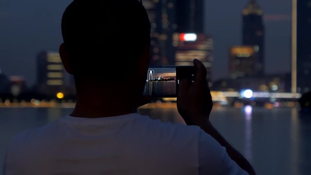 28 june, 2018. China, Suzhou city, Jinji Lake. Adult man make a photo of beautiful sunset cityscape by smartphone
