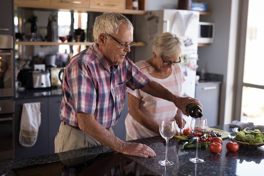 Senior man pouring wine into glass at home