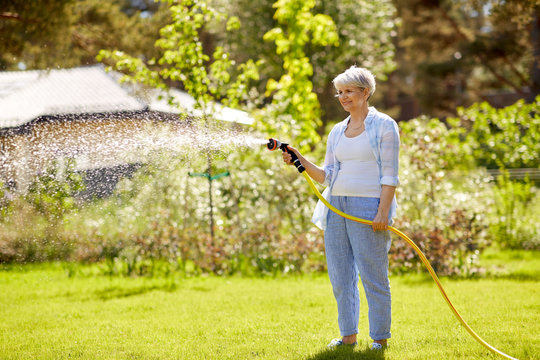 Gardening And People Concept - Happy Senior Woman Watering Lawn By Garden Hose At Summer