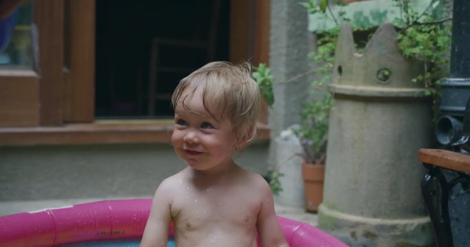 Little toddler boy in paddling pool outside