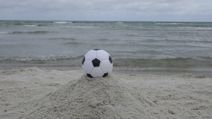 Ein schwarz-weißer Fußball liegt am Strand mit dem Meer im Hintergrund,  Nahaufnahme 