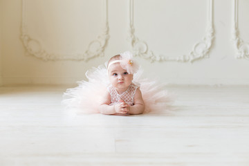 Baby girl wearing a peach tutu. Cute smiling baby girl lying on the floor on creamy background