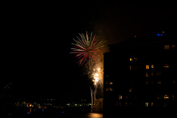 A Fourth of July fireworks display explodes over the waterfront in the city center of Norfolk Virginia, in the context of buildings, apartments, and dwellings