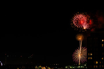 A Fourth of July fireworks display explodes over the waterfront in the city center of Norfolk Virginia, in the context of buildings, apartments, and dwellings
