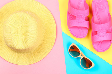 Hat, sunglasses and slippers on a three-color pastel background of blue, yellow and pink.