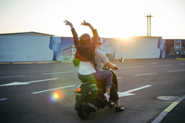 Happy young couple riding vintage scooter on urban background and having some fun
