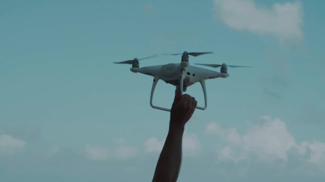 Male hand catching drone against blue summer sky background - video in slow motion