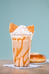 Delicious fresh milk and ice cream with whipped cream and cookie in glass on table with cheesecake on blue background