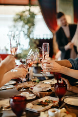 Crop view of anonymous people enjoying time clinking glasses with champagne over table in restaurant