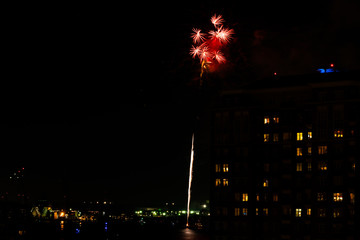 A Fourth of July fireworks display explodes over the waterfront in the city center of Norfolk Virginia, in the context of buildings, apartments, and dwellings