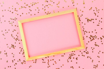 A wooden empty frame on a pastel background surrounded by shiny decorative stars and balls.