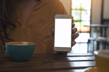 Mockup image of a woman holding and showing white mobile phone with blank desktop screen with coffee cup on wooden table