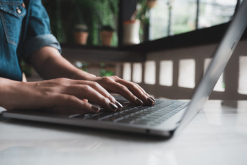 Closeup image of a woman's hands working and typing on laptop keyboard on table