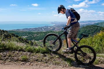 Young male mountain biker on an electric bicycle balancing on the border of a mountain road,...