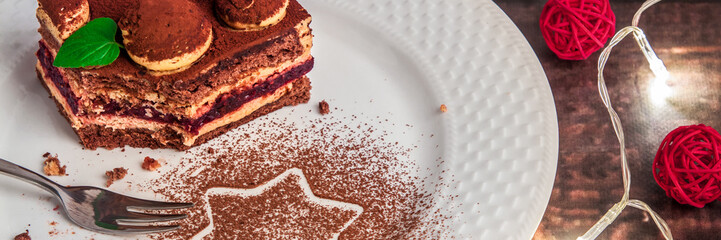 Panoramic view on tiramisu on a white plate with cocoa, fork, Christmas lights and red decorative balls
