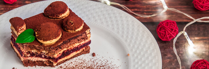 Panoramic view on tiramisu on a white plate with cocoa, Christmas lights and red decorative balls