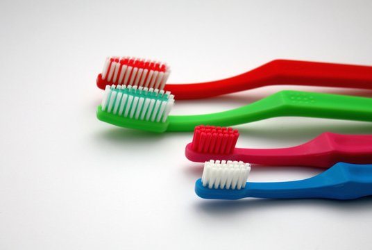 Colorful family toothbrushes on white background, red and green adult toothbrushes and pink and blue little two for children.