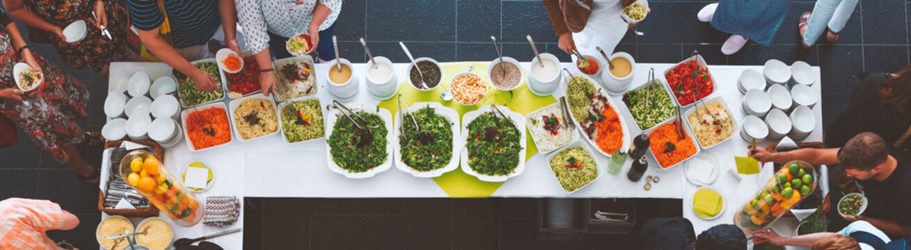 Großes vegetarisches Catering Salat  Buffet mit gesundem Essen, Salten und Obs wo sich Menschen bedienen 