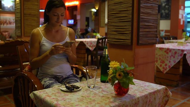 A woman sitting in a restaurant takes pictures of fried insects on a plate. Thai food.