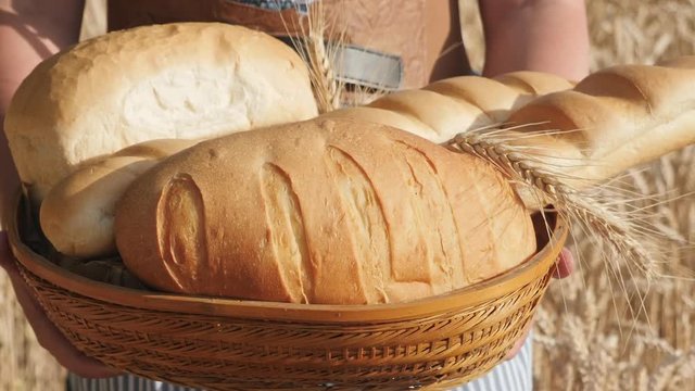 A woman carries a basket of freshly baked bread, walking along a ripe wheat fie. Close-up shot. Slow motion video