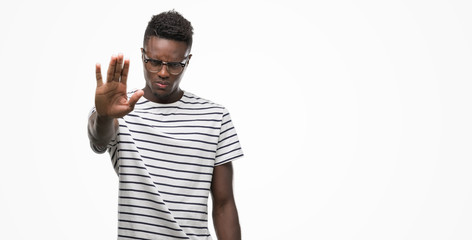 Fototapeta premium Young african american man wearing glasses and navy t-shirt doing stop sing with palm of the hand. Warning expression with negative and serious gesture on the face.