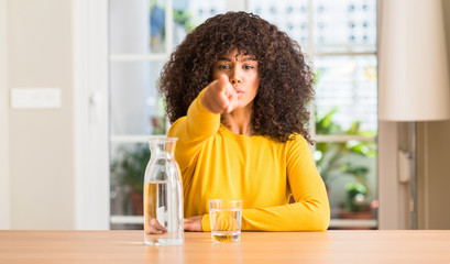 African american woman drinking a glass of water at home pointing with finger to the camera and to you, hand sign, positive and confident gesture from the front