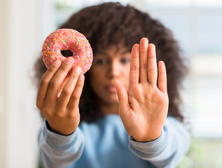African american woman holding donut at home with open hand doing stop sign with serious and...