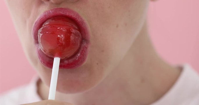 Crop face of beautiful young woman with lollipop close-up on a pink background