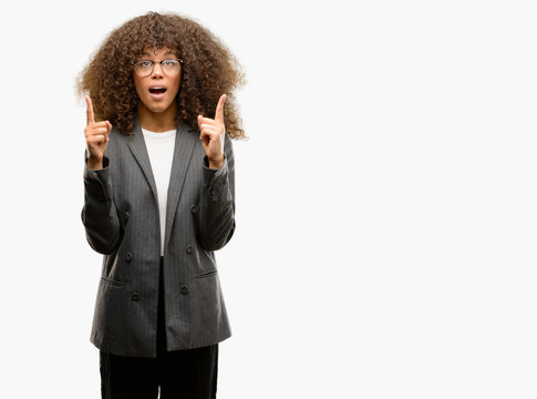 African american business woman wearing glasses amazed and surprised looking up and pointing with fingers and raised arms.